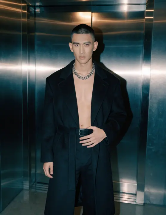 Long black coat and silver chain in a steel elevator